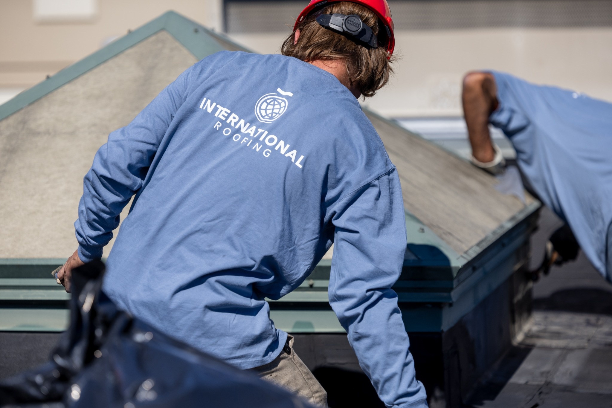 Two roofers in blue shirts and red hard hats working